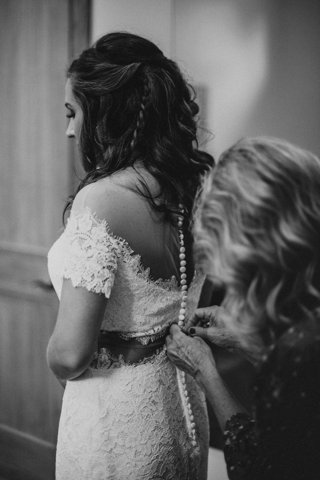 Mother buttoning up Bride's wedding dress