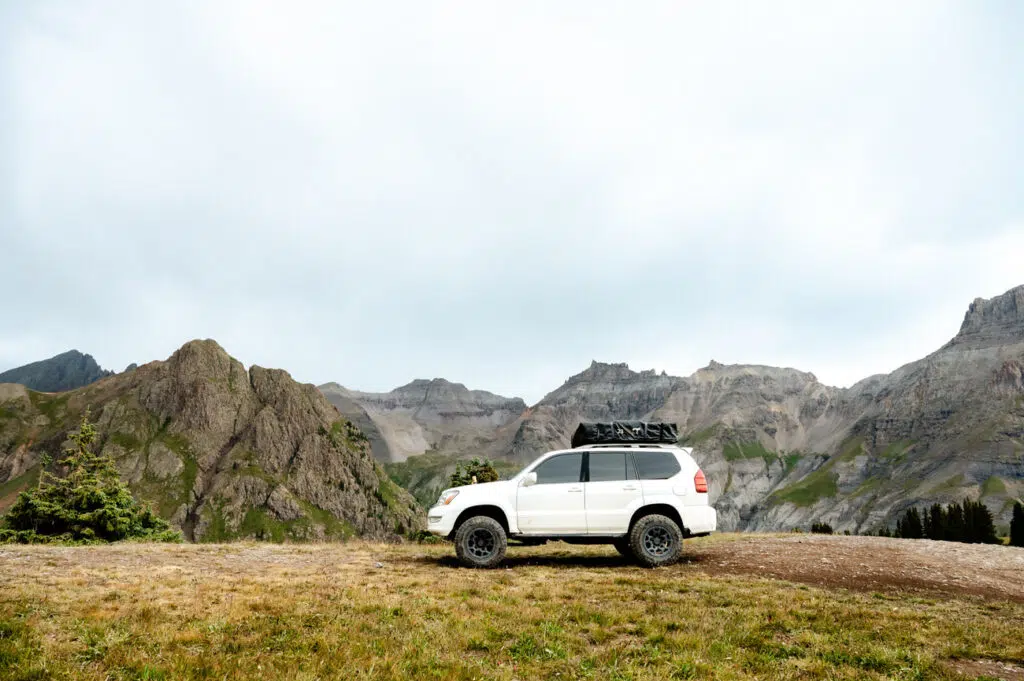 a white car parked on a grassy hill with mountains in the background
