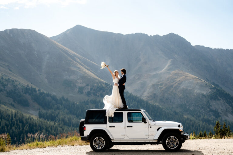 a bride and groom in wedding attire on top of a jeep eloping in Colorado