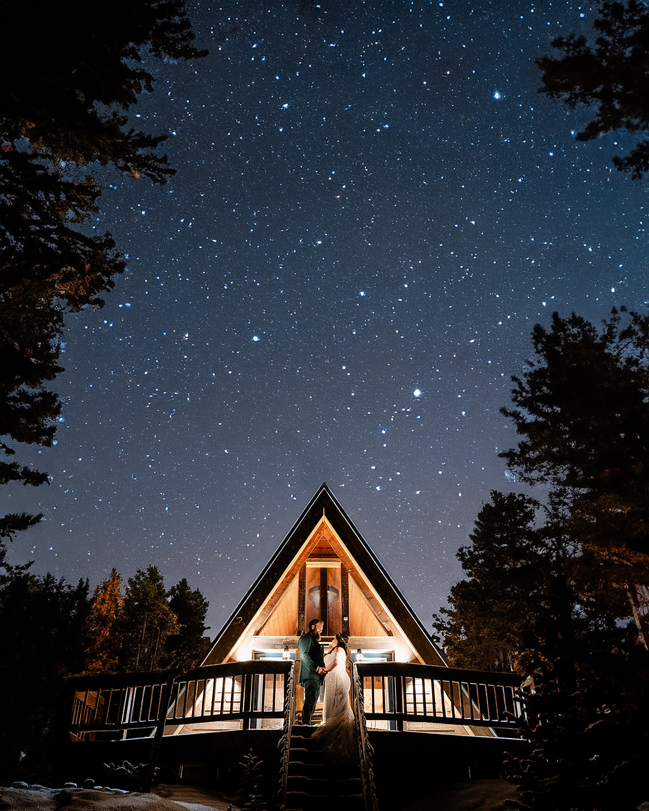 a couple standing on a deck in front of an AirBnB wedding venue with trees and stars in the sky