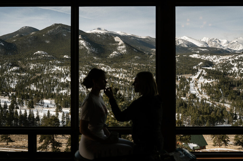 bride having hair and makeup done in AirBnB on wedding day with mountains in the background